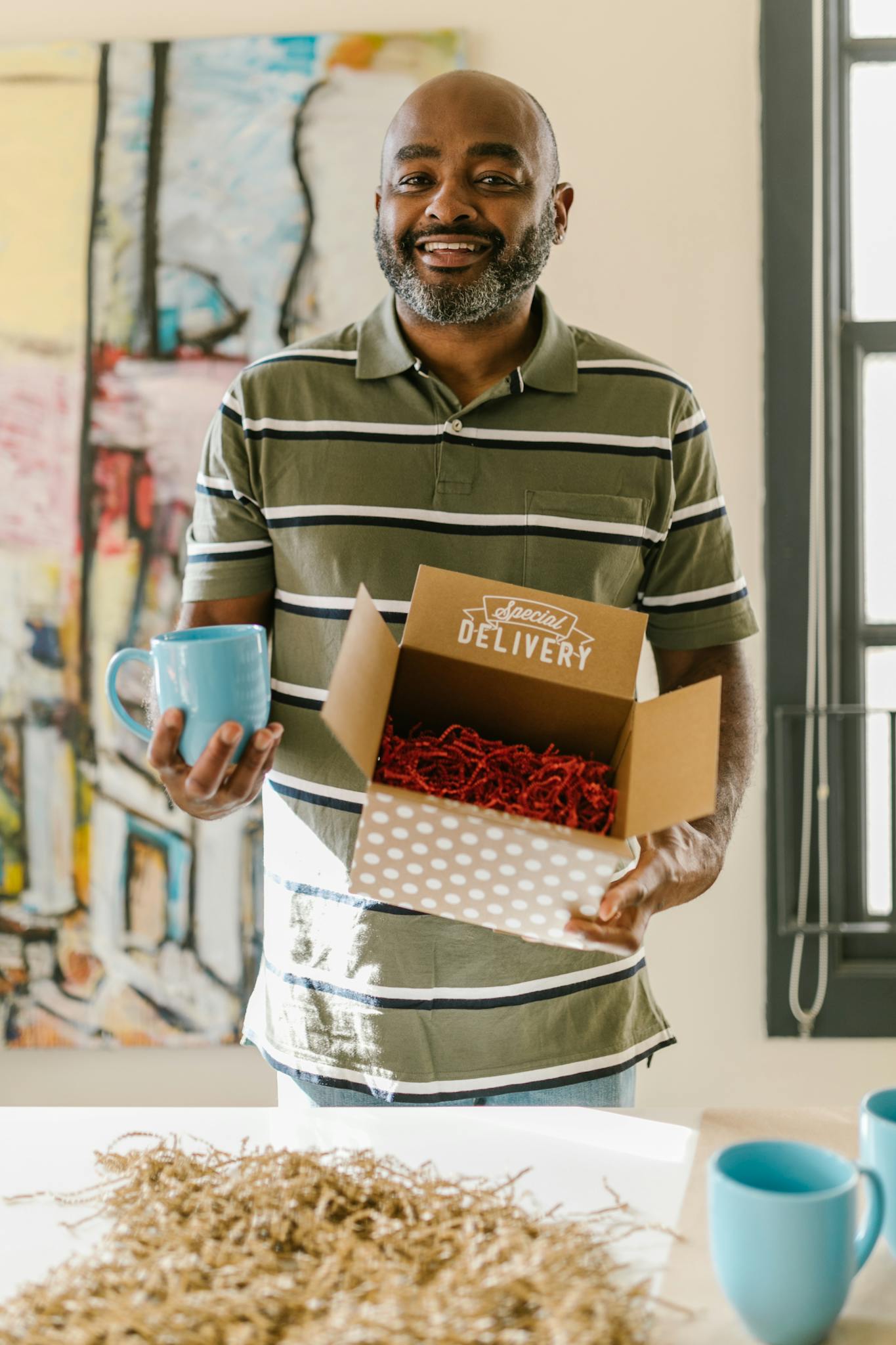 Entrepreneur holding a delivery box and mug, showcasing a small business environment.