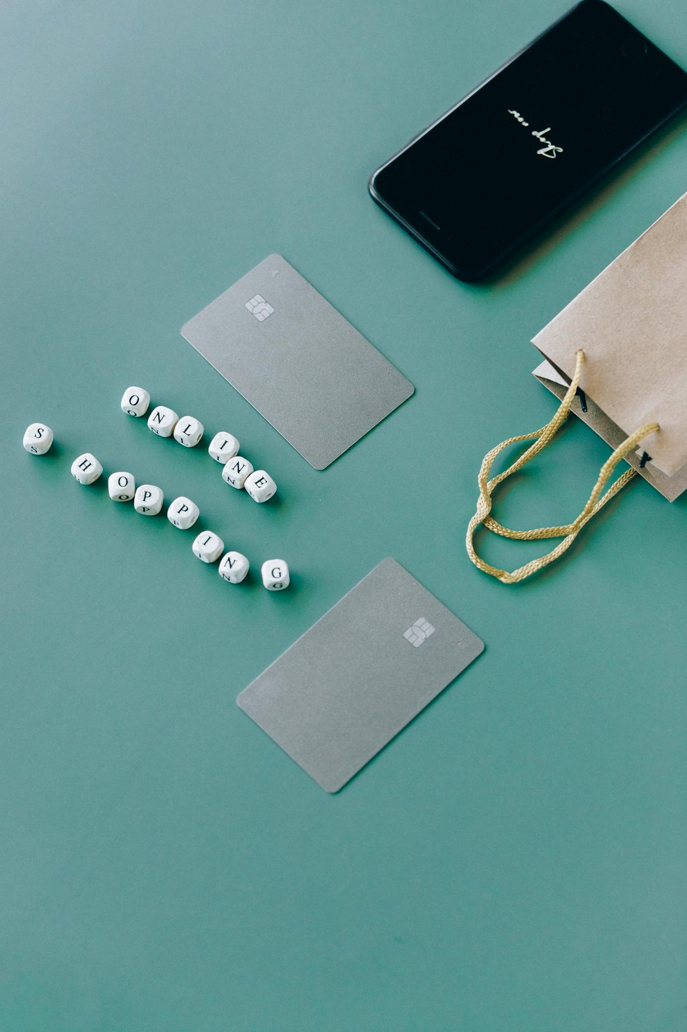 Top view of bank cards, smartphone, and shopping bag on green surface, illustrating online shopping.